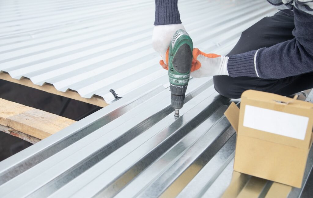 Man installing metal sheet roof by electrical drilling machine.