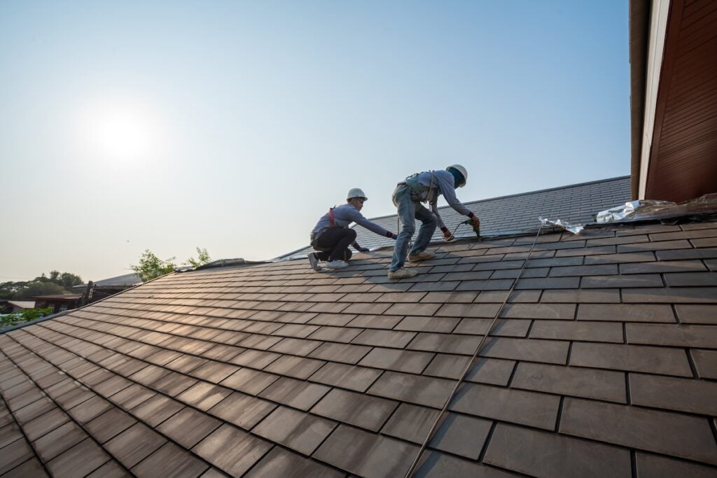 Roofer worker in special protective work wear and gloves,Using pneumatic gun and repair and replace roof tile on top of the new roof.