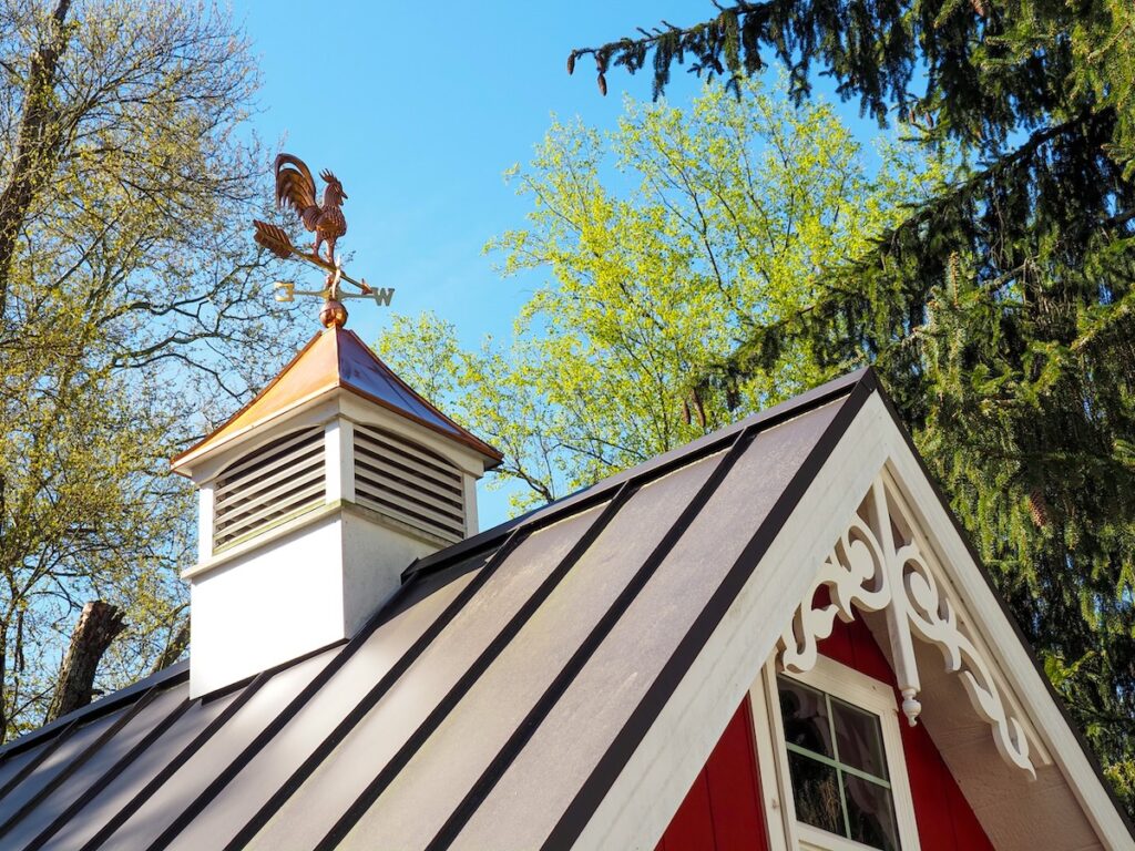 Copper rooster weathervane and cupola on red shed or barn with dark metal roof