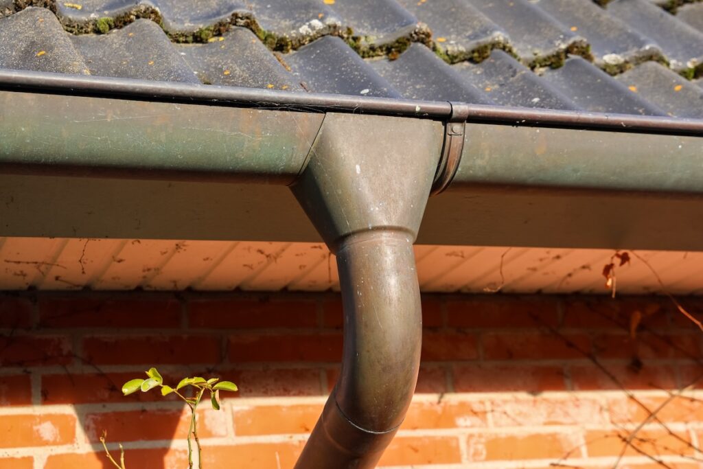 Old metallic gutter and downspout collecting rainwater from a tiled roof